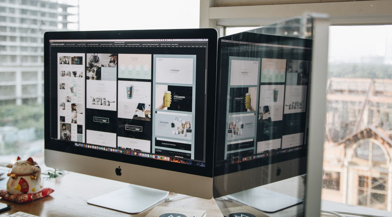 Two monitors on a desk, displaying web design work in a contemporary office environment.
